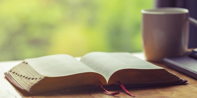 open Bible on table next to coffee mug by window