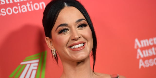 Katy Perry flashes a smile on the red carpet in a gown with her hair pulled back