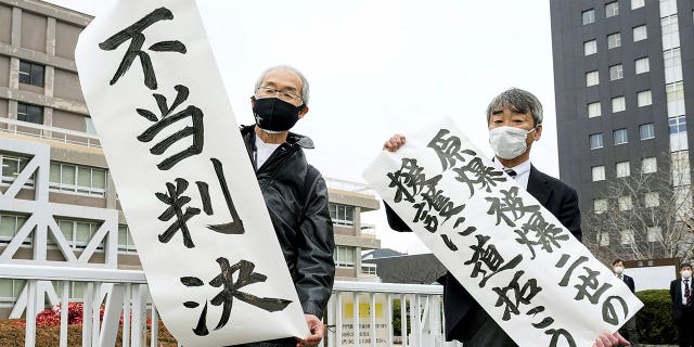 Plaintiff Katsuhiro Hirano, right, and an unidentified lawyer for the plaintiffs display signs in Hiroshima, Japan, on Feb. 7, 2023. The banners read "Pave the way to backup Second-Generation Atomic Bomb Survivors," right, and "Unfair judgement."