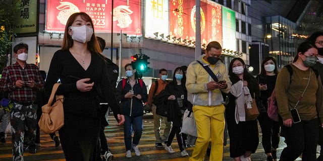 People wearing face masks walk across a busy street at the Causeway Bay shopping district in Hong Kong, on Feb. 7, 2023. 
