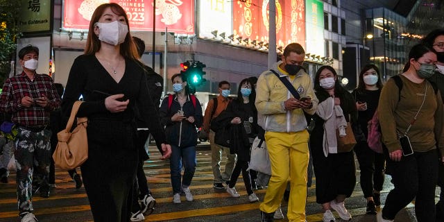 People wearing face masks walk across a busy street at the Causeway Bay shopping district in Hong Kong, on Feb. 7, 2023. 