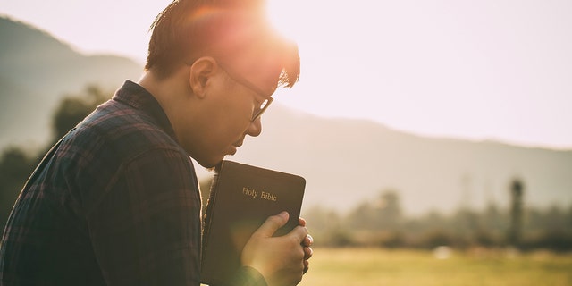 man praying while holding bible