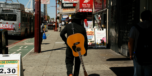 A man with a guitar is looking for a music venue in the Mission District of San Francisco.