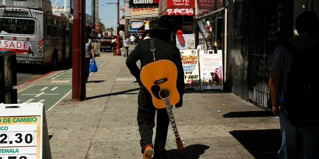 A man carrying a guitar looks for a place to play music in the Mission District in San Francisco.