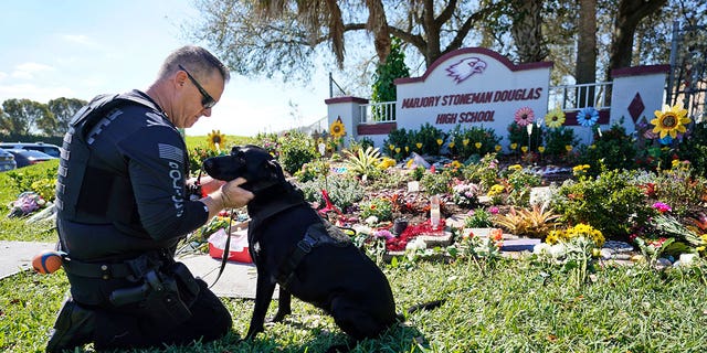 Coconut Creek, Fla., police officer Michael Leonard takes a moment with his School Safety Dog Taylor, Tuesday, Feb. 14, 2023, as he visits a memorial in front of Marjory Stoneman Douglas High School (MSD) in Parkland, Fla. Leonard was the officer that stopped and arrested Nikolas Cruz after Cruz fled after he opened fire on students and staff at MSD on Valentine's Day in 2018, killing 17. 