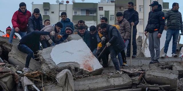 Men search for people among the rubble at a destroyed building in Adana, Turkey on Monday, February 6, 2023. A powerful earthquake has knocked down several buildings in southeast Turkey and Syria and many are feared dead.