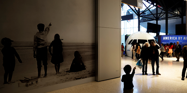 A child points at a group of patrons touring an exhibit at the Smithsonian National Air and Space Museum.