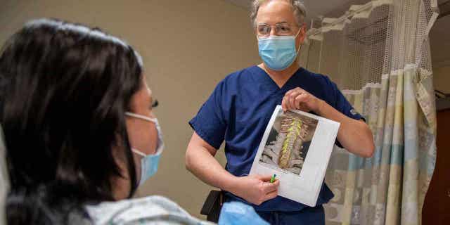 Dr. Peter Gerszten tells study participant Heather Rendulic how electrodes will be implanted on her spinal cord at UPMC Presbyterian in Pittsburgh on May 7, 2021.