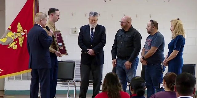 Former Virginia Senator Jim Webb presents a plaque and a missing dog tag belonging to late USMC Corporal Larry Hughes to the veteran's family.