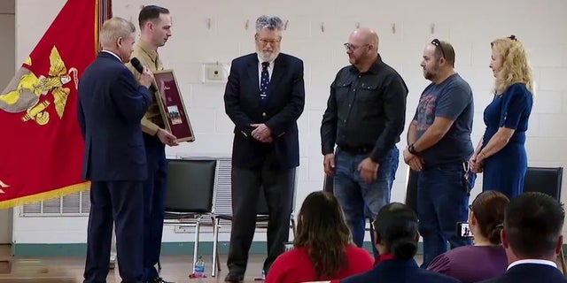 Former Virginia Senator Jim Webb presents a plaque and a missing dog tag belonging to late USMC Corporal Larry Hughes to the veteran's family.