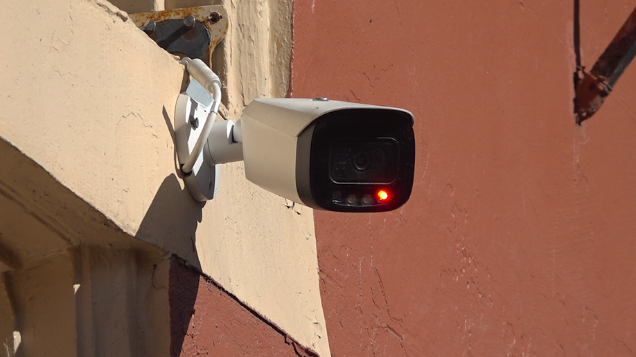 Security camera blinking, hanging on the outside wall of a building