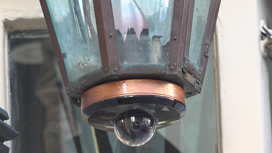 Camera discreetly placed at the bottom of a light chandelier hanging outside a storefront