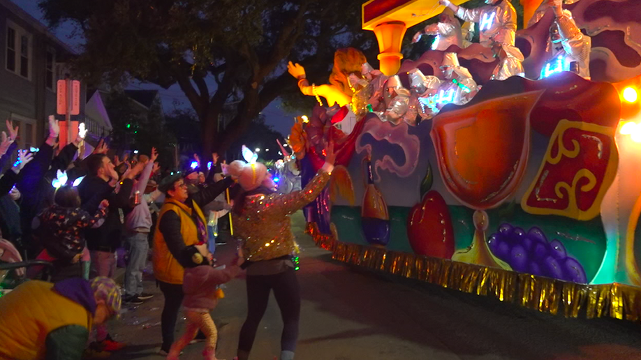 People in costume throwing beads off a float to the crowd 