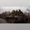 A group of military men ride on a tank.