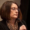 A woman speaks into a microphone while on the witness stand inside a courtroom.