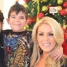 Slade Smiley in a black zip-up and red button down smiles for a photo next to son Grayson in a printed graphic shirt with arms wrapped around Slade and Christine Rossi, who is wearing a sparkly gold shirt and black sweater