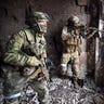 Two soldiers hold guns while patrolling war wreckage.