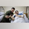 A man in a hospital bed smiles and gives a thumbs up with another man.
