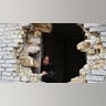 A woman peers out of a large hole in the side of her house.