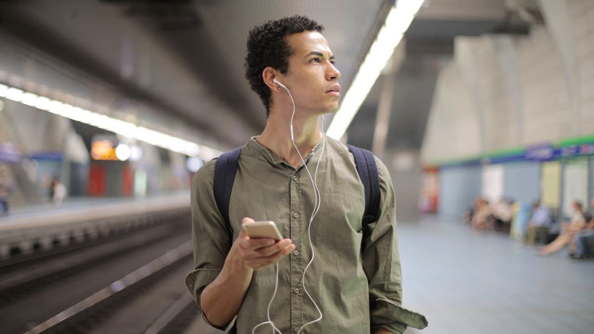 Man standing in a subway station with his phone out.
