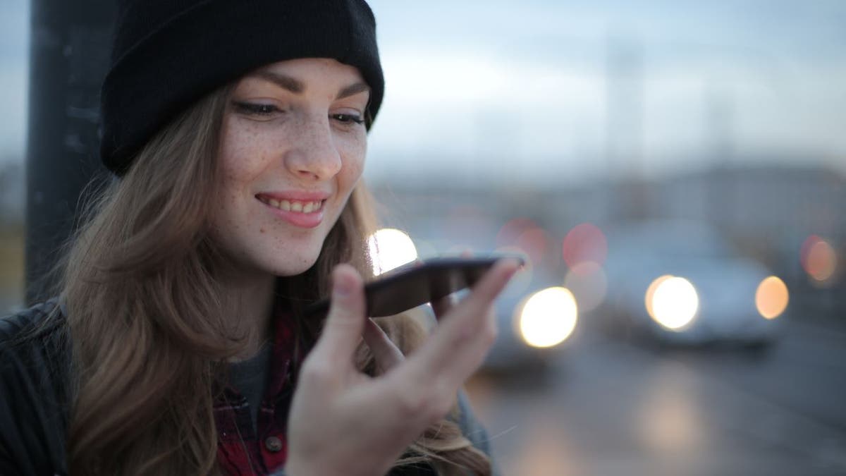 Woman smiles as she answers her phone on speaker