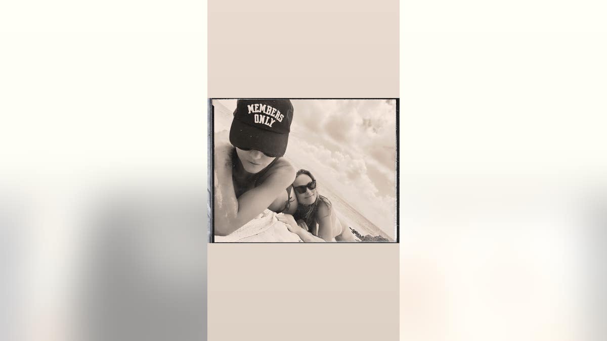 Molly Howard wears a Members Only hat with Olivia Wilde in a white bikini