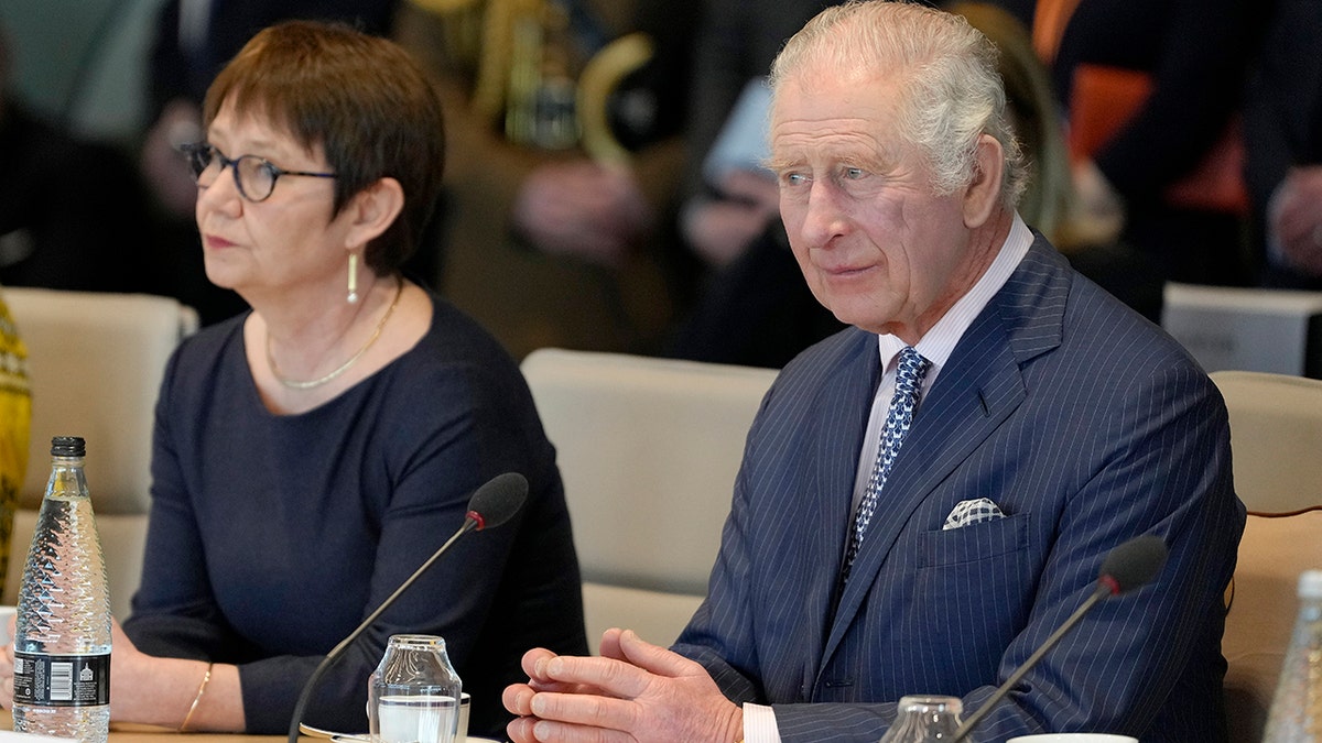 King Charles looking serious in a blue suit attending a conference