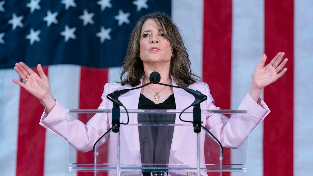 Marianne Williamson arms lifted, US flag behind her