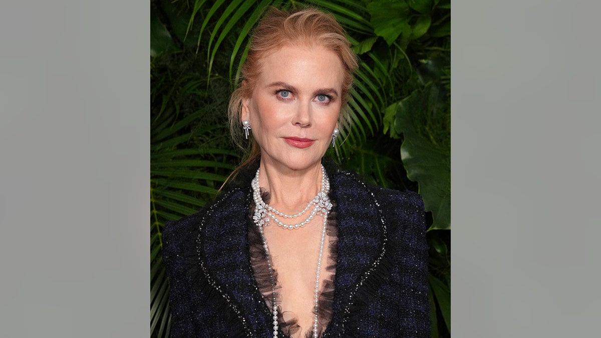 Nicole Kidman wears a navy blue and black tweed jacket with no bra underneath and a long pearl necklace