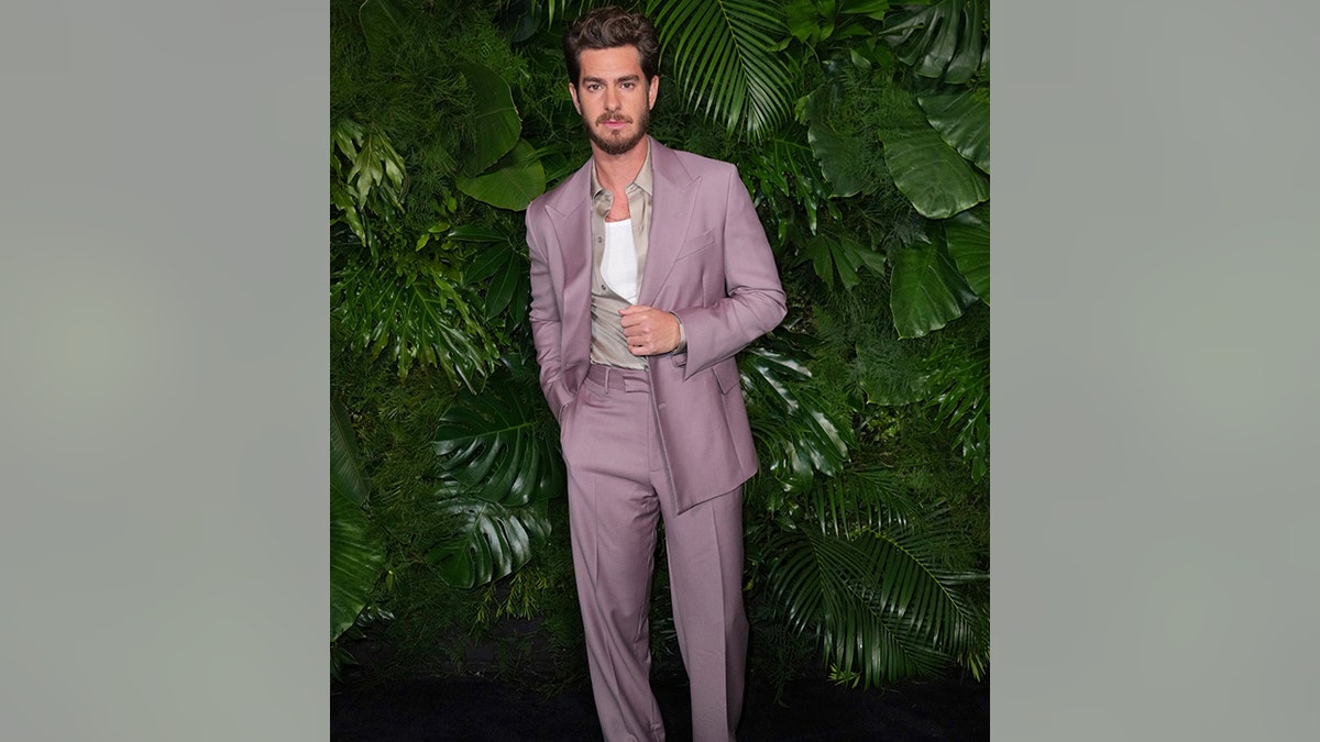 Andrew Garfield in a lavender suit and pants with a white undershirt and grey button down at the Chanel and Charles Finch dinner