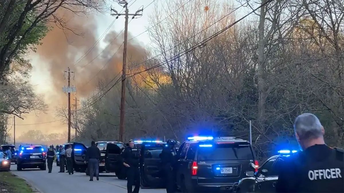 police cars on road, smoke rising in background