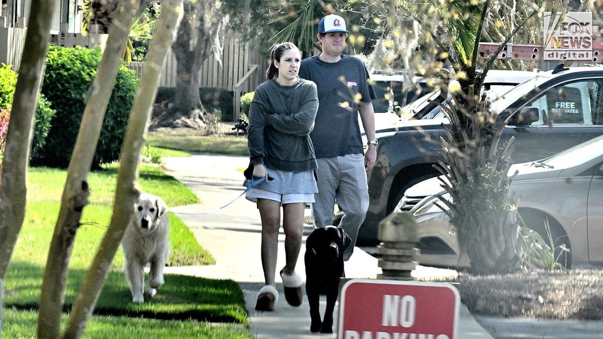Brooklynn wears shorts and a long sleeve top, Buster is wearing pants and a Vineyard Vines t-shirt, they are walking two dogs on leashes