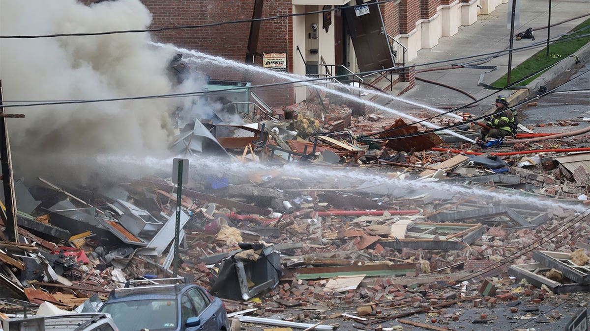 Firefighter sitting on the debris spraying the firehose as the fire subsides.