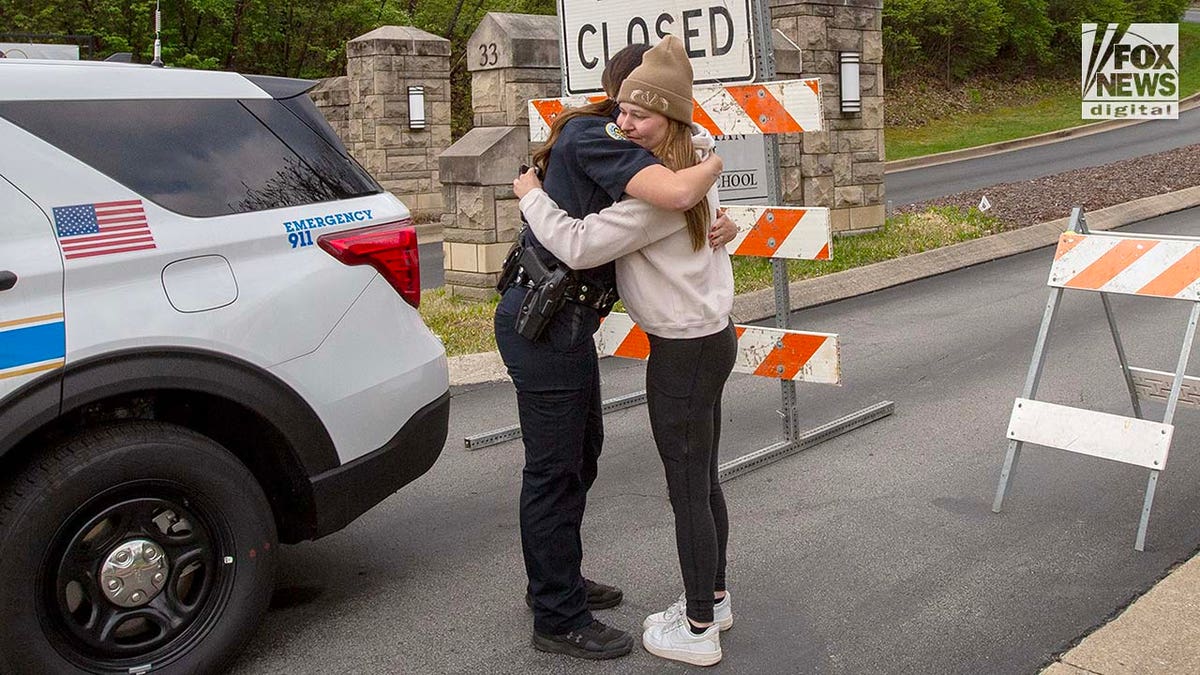 A police officer comforts a mourner outside of The Covenant School