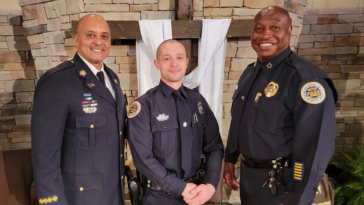 Three uniformed men stand posed up in front of a Christian cross