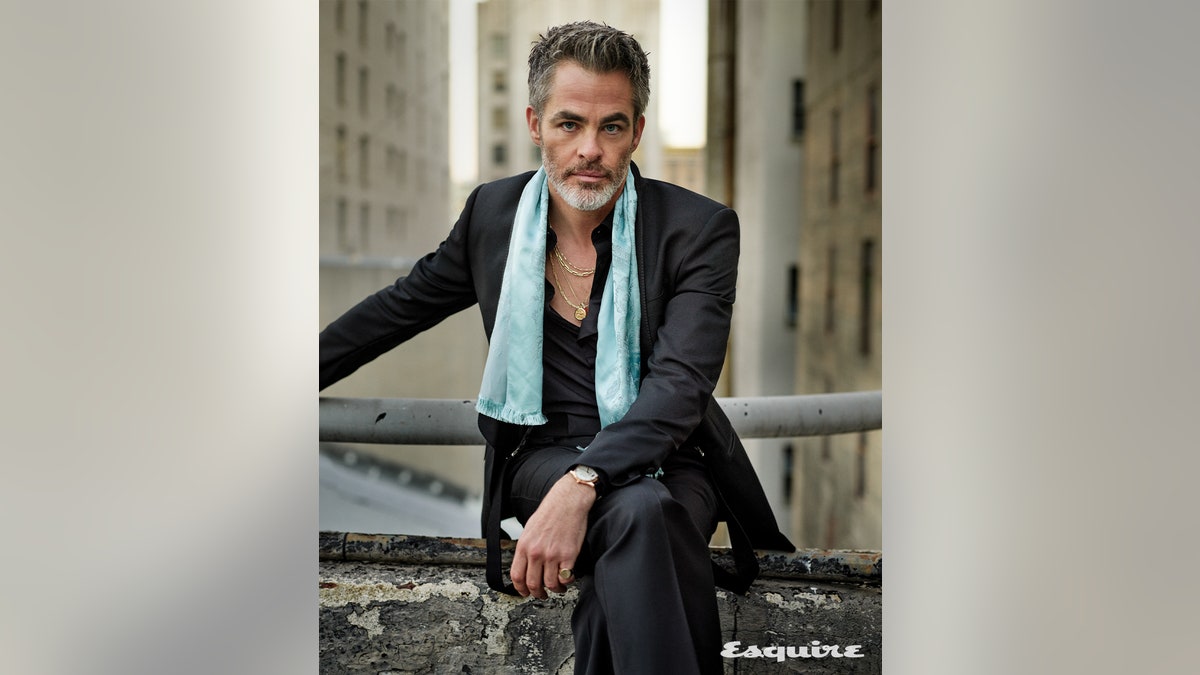 Chris Pine wears a grey suit and light blue scarf while posing for Esquire