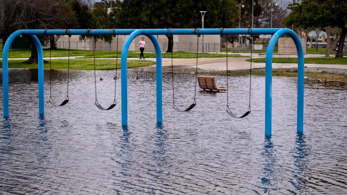 A person walks past a flooded playground in Huntington Beach