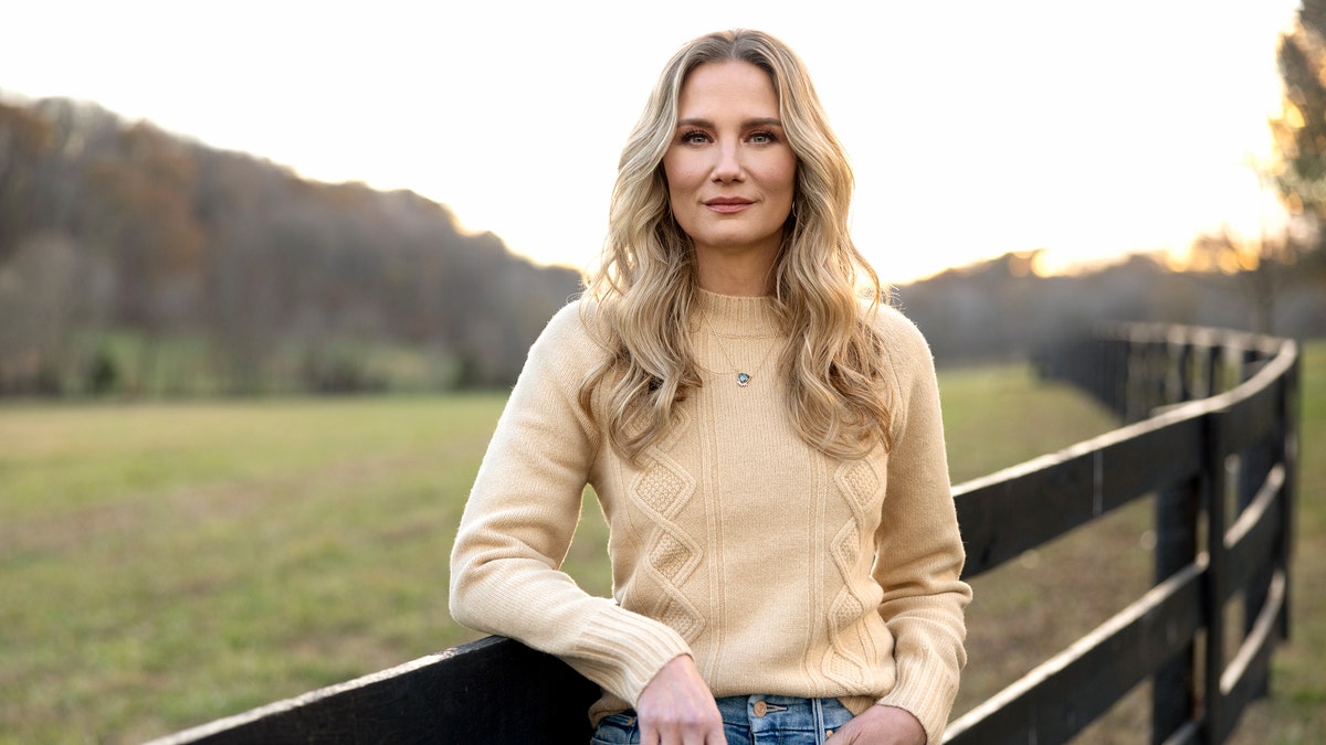 Jennifer Nettles wears a sweater and jeans next to a fence