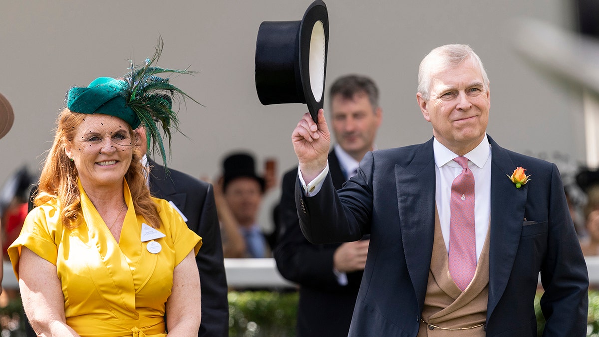 Sarah Ferguson in a bright mustard colored dress and green feathered hat smiles next to Prince Andrew tipping his top hat wearing a suit and red tie