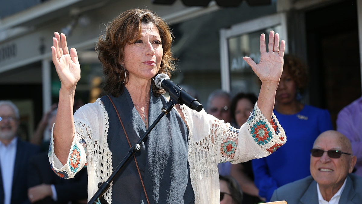 AMy Grant holding her hands up in prayer wearing white top and gray scarf