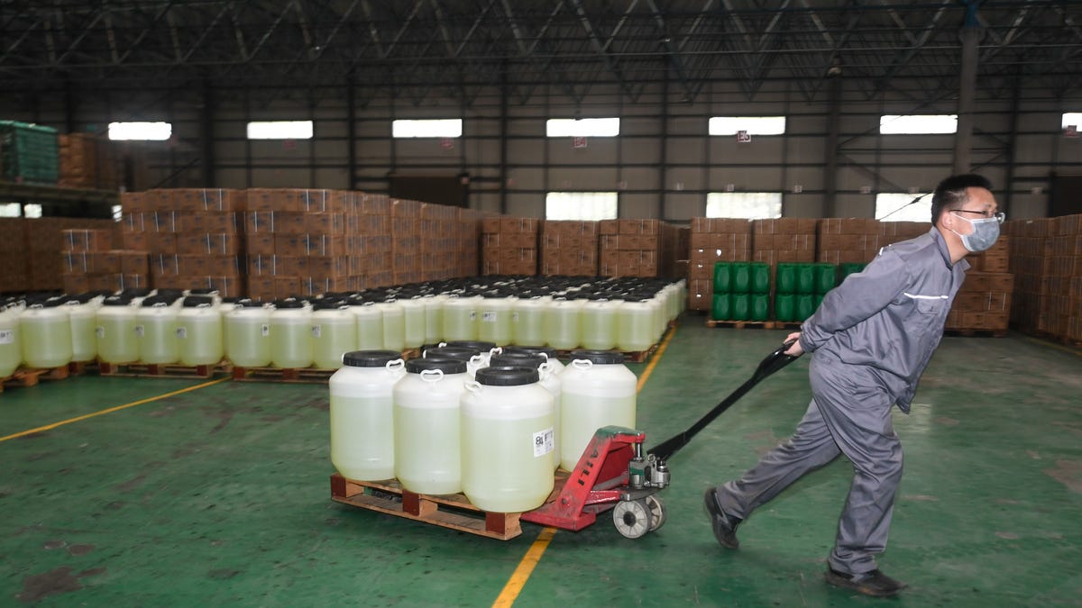 Chinese factory worker pulling cart full of large antiseptic solution containers. 
