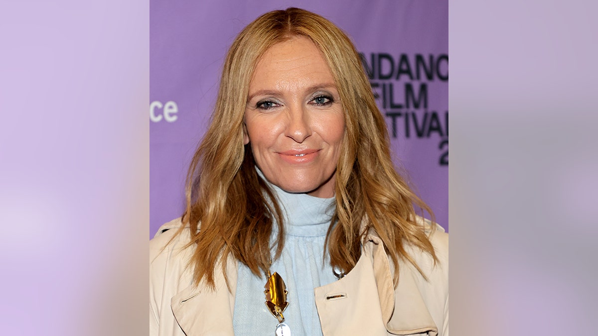 Toni Collette in a light blue turtleneck and tan jacket soft smiles on the red carpet in Salt Lake City, Utah