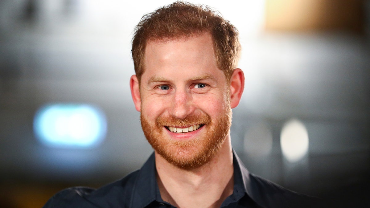 Prince Harry wears a black shirt smiles off camera in London