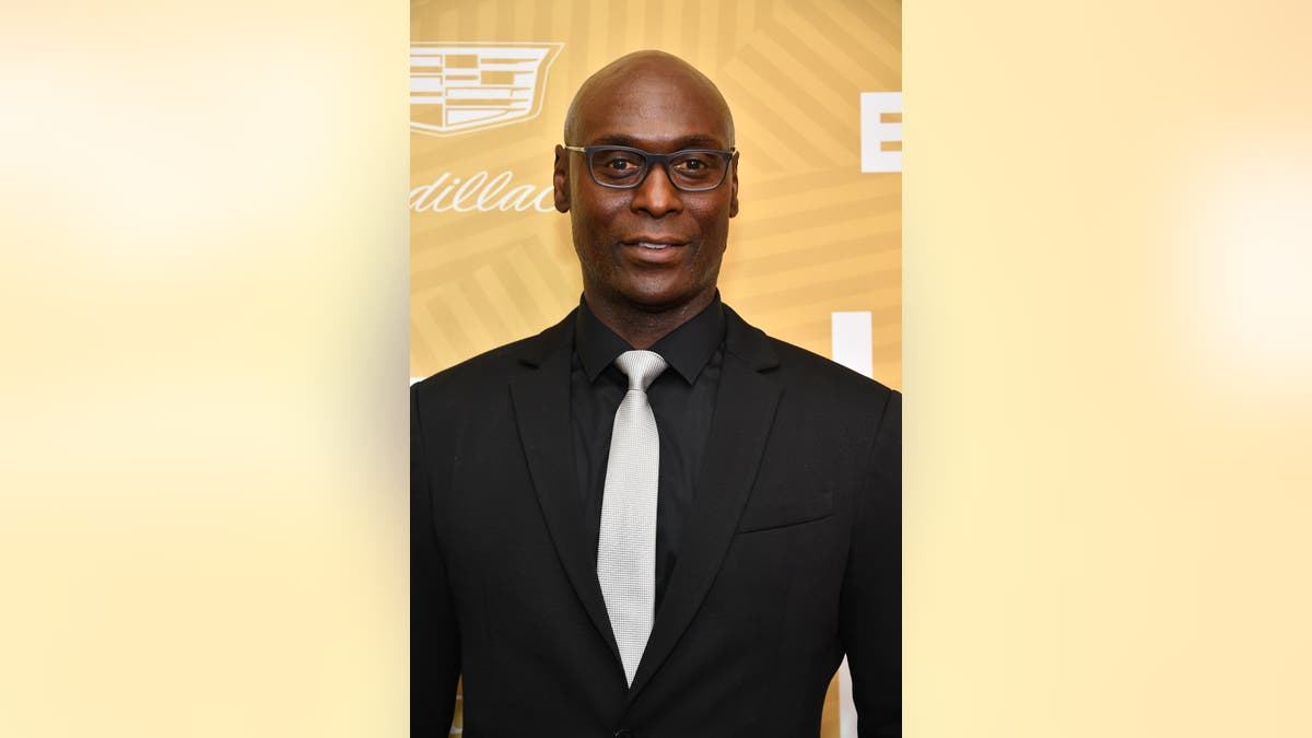 Lance Reddick walks red carpet wearing black suit and white tie