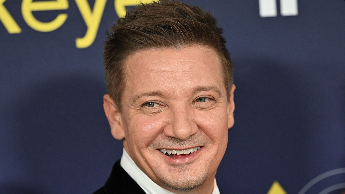 Jeremy Renner looks back and smiles, off-camera on the red carpet