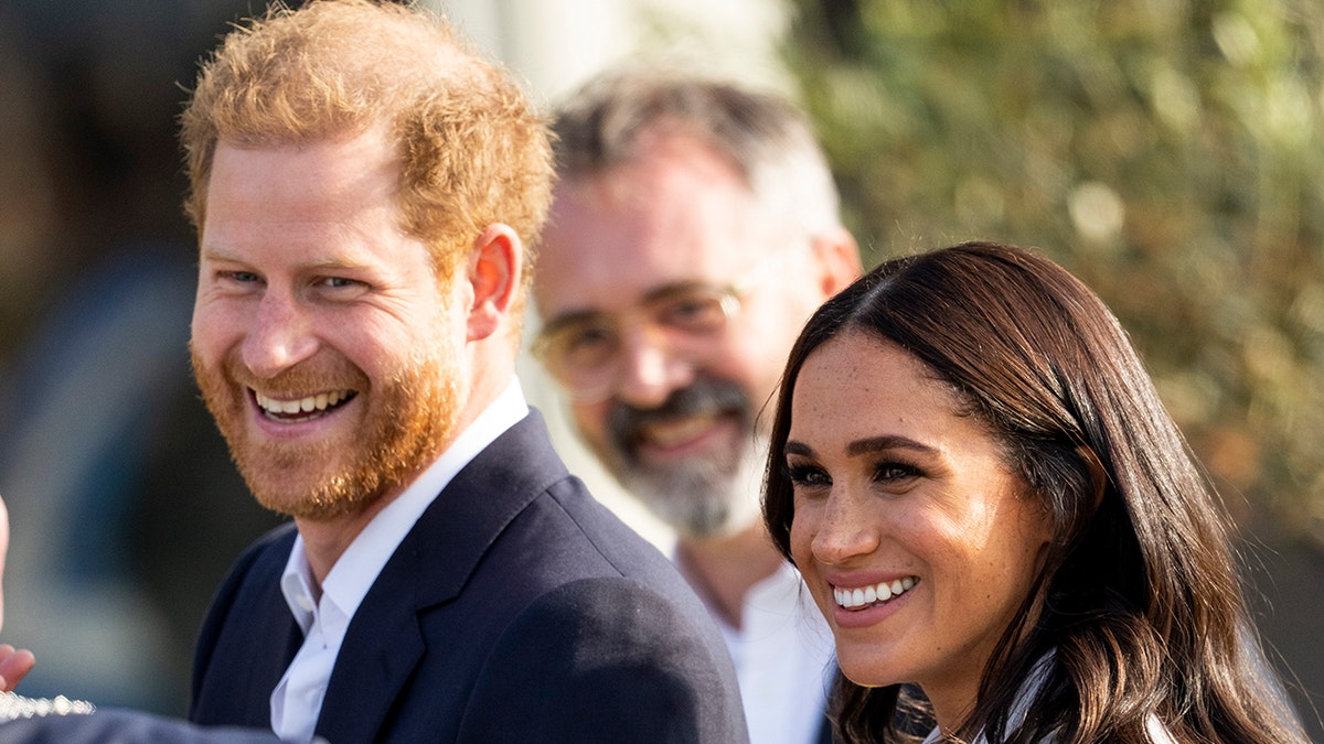 Prince Harry in a blue button down shirt and black suit smiles with wife Meghan Markle in the Netherlands for the Invictus Games