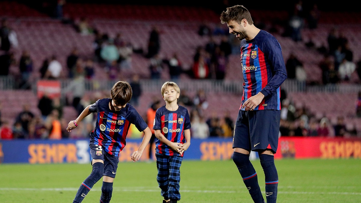 Gerard Piqué with his sons Milan and Sasha, all wearing FC Barcelona gear, kicking the soccer ball around on the field