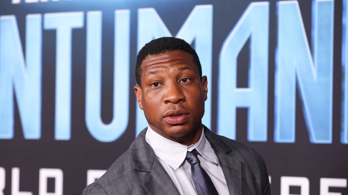 Jonathan Majors in a grey suit, white button down shirt and blue tie on the red carpet for "Ant-Man and The Wasp: Quantumania"