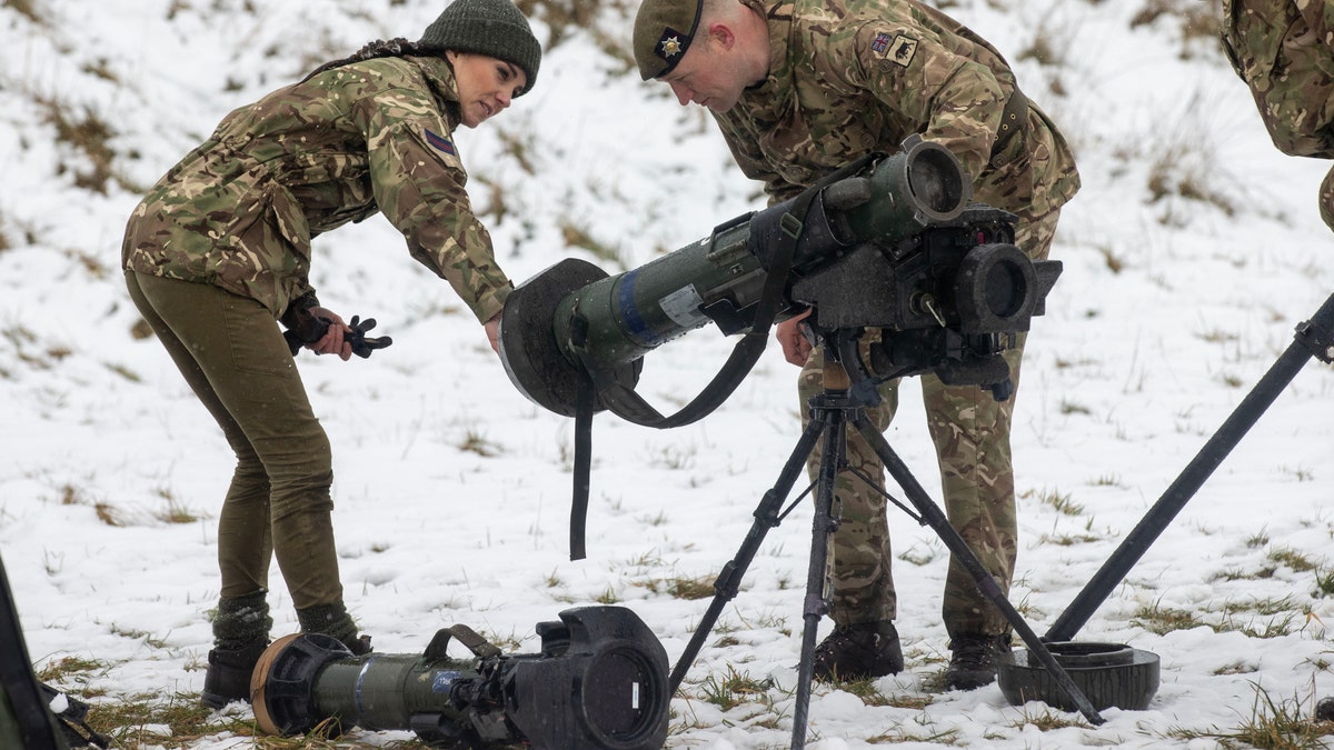 Kate Middleton in camo gear and soldier working with military weapon