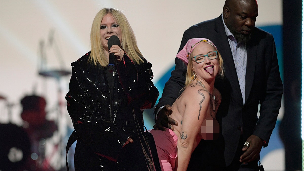 topless protestor sticks her tongue out and poses on stage next to avril lavigne